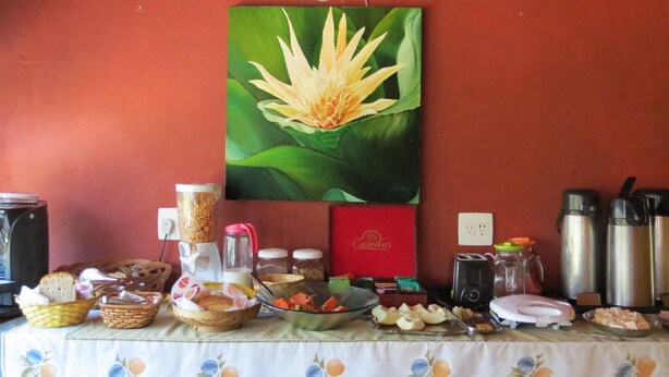 Een ontbijtbuffet met diverse soorten eten, een koffieapparaat, en een schilderij van een lotusbloem aan de muur.