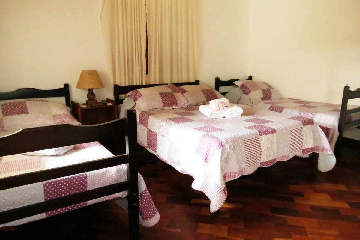 Una habitación con dos camas, cada una con colcha y almohadas a cuadros. Entre las camas, una mesita de noche con lámpara.