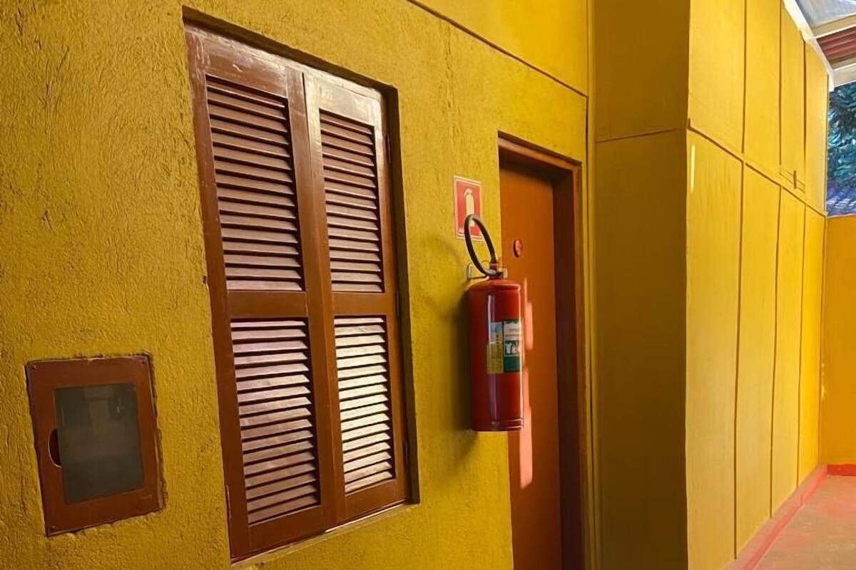 Un pasillo con paredes amarillas, un extintor de incendios sujeto a la pared y una puerta con un ventanal.