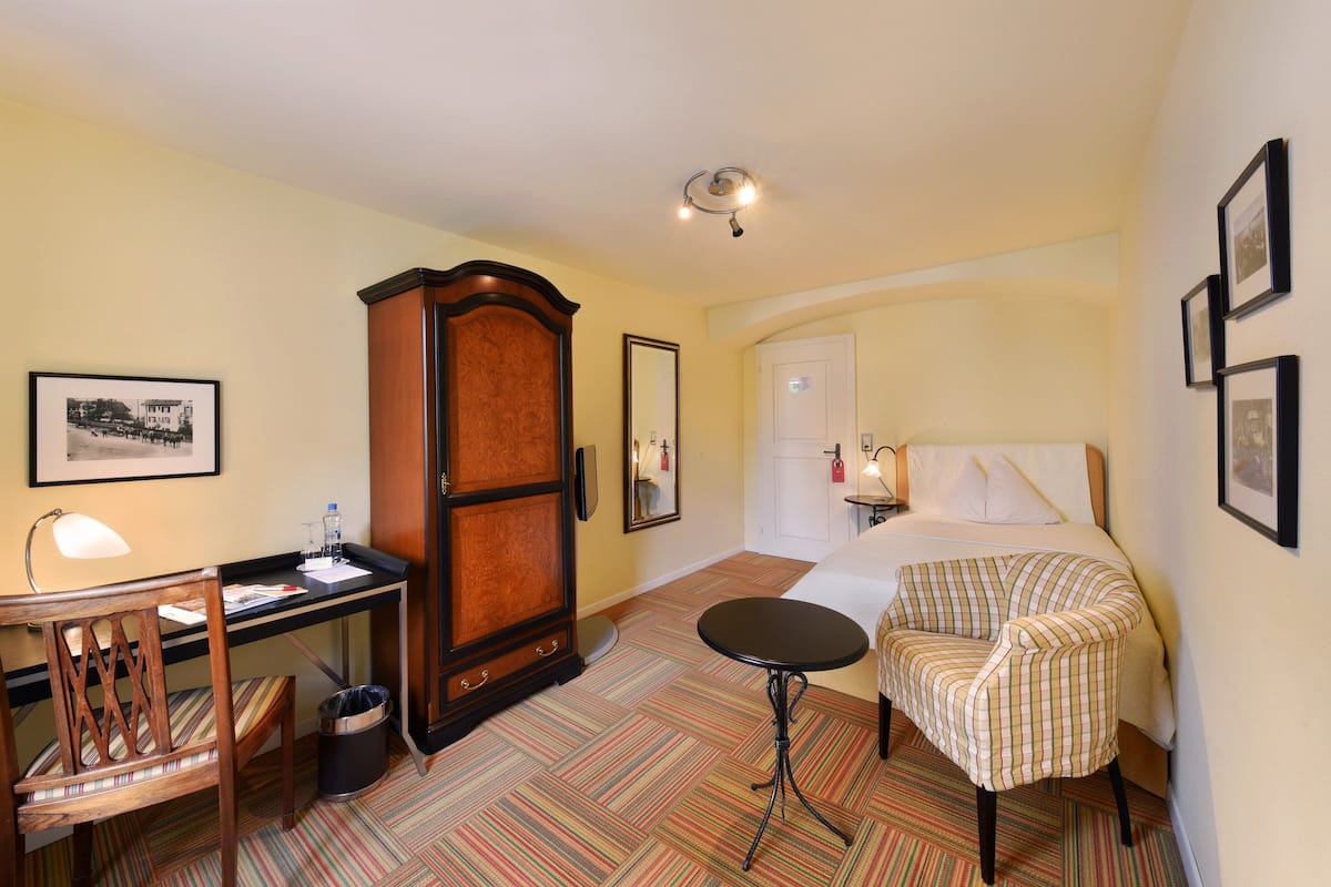 A hotel room with a bed, a desk, a chair, a small table, and a cabinet.