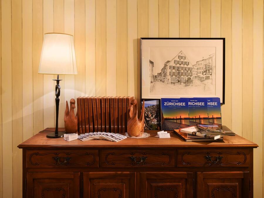 Et træbord med en lampe, en vase, et indrammet bybillede og en bog med titlen "Zürichsee".
