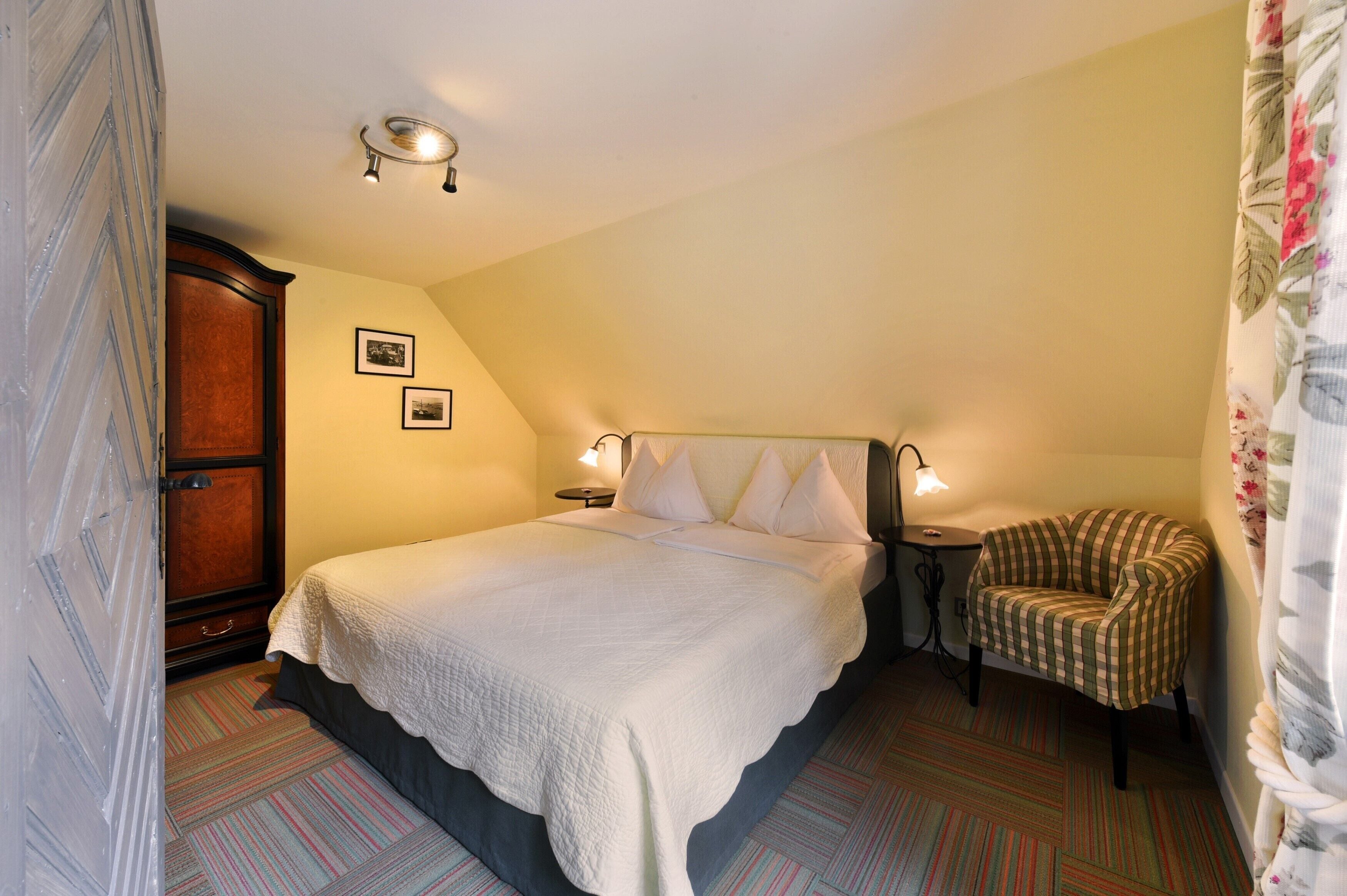 Een keurig opgemaakt slaapkamer met een groot bed, een klein nachtkastje, een stoel en een kledingkast.