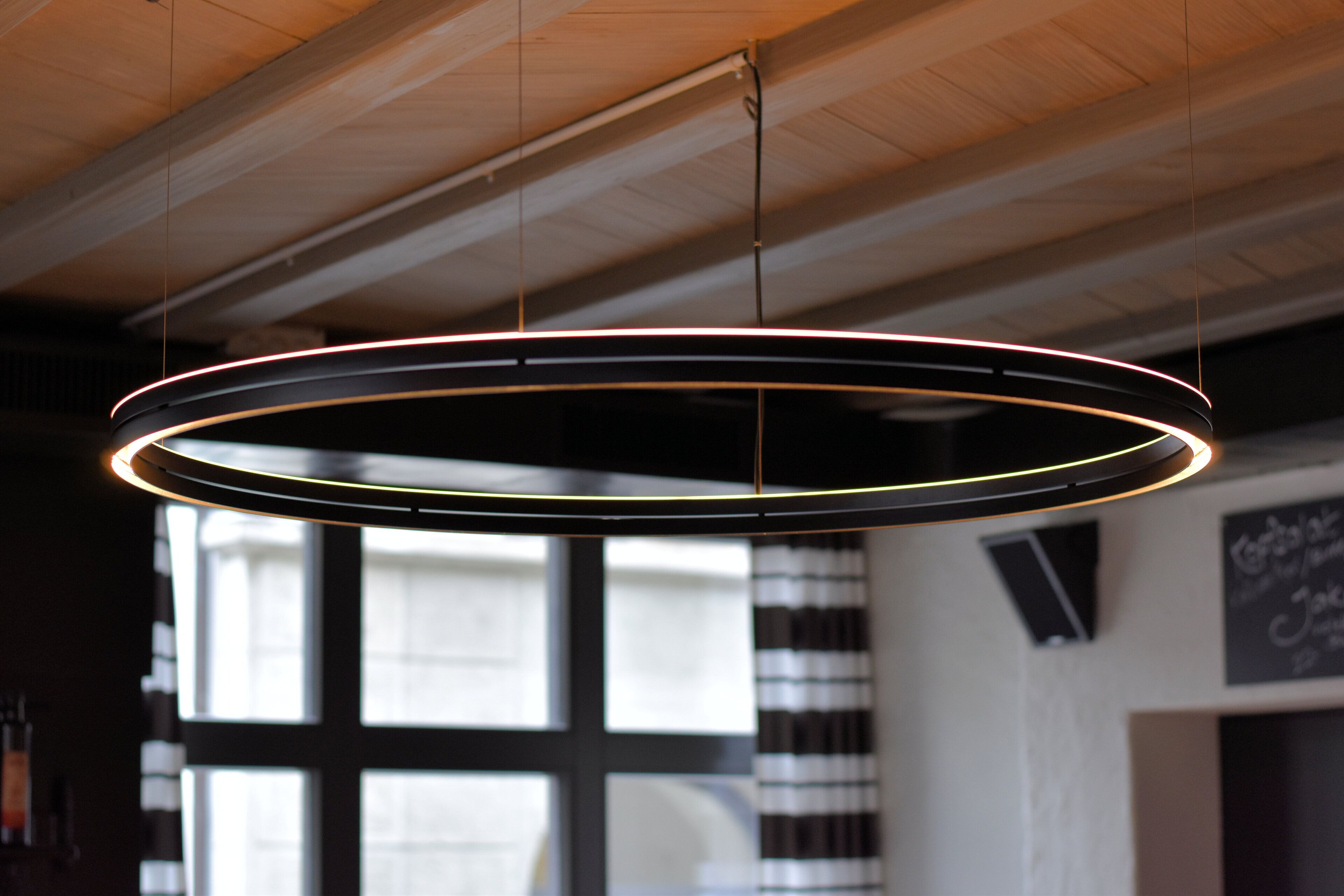 A circular light fixture with a glowing ring design, suspended from a ceiling with visible wooden beams.