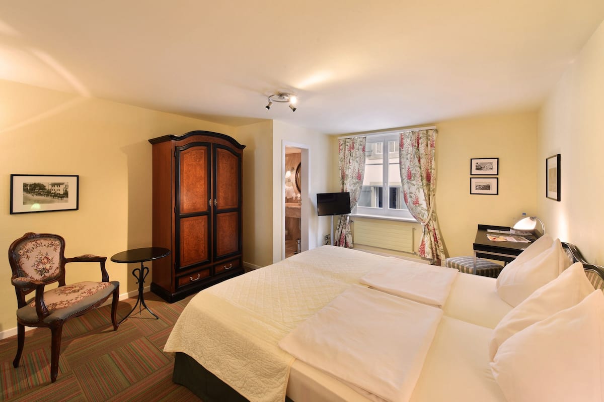 A hotel room with a large bed, a wooden wardrobe, a small table, a chair, and a television.