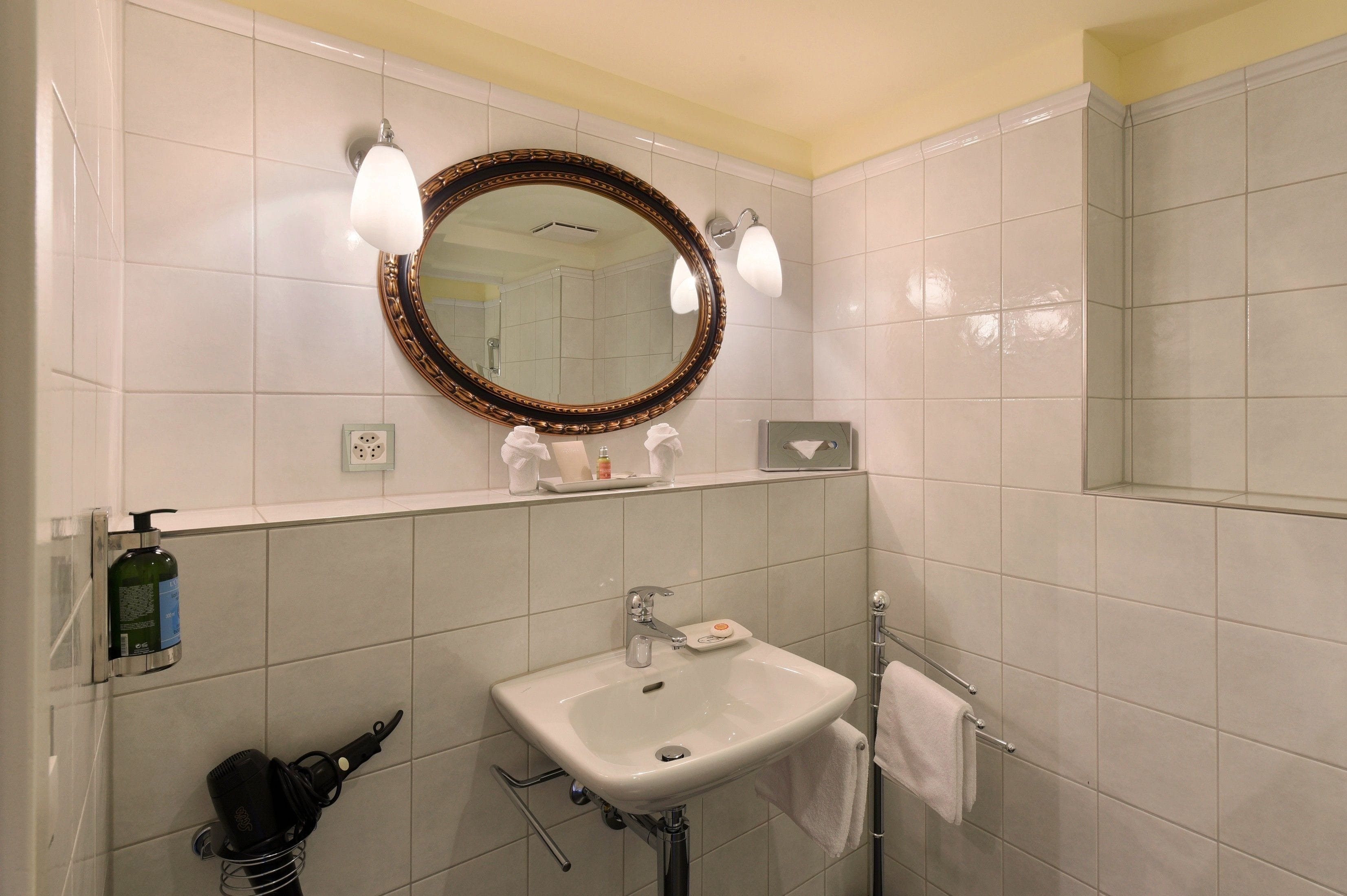 A bathroom with a white sink, a mirror with a decorative frame, and a towel rack.