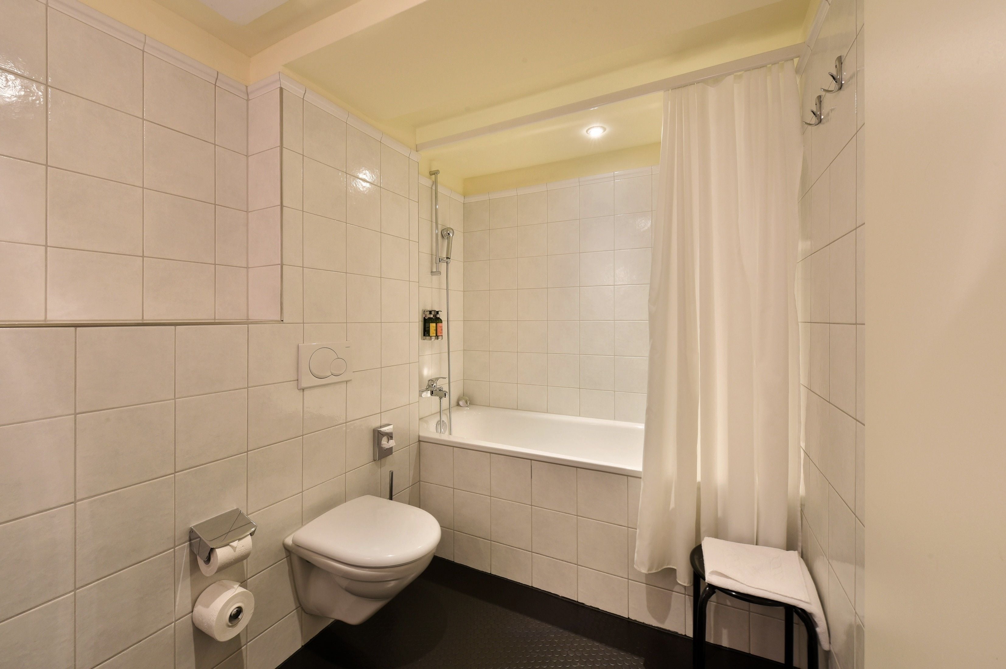 A bathroom with white tiles, a toilet, a bathtub, and a shower.