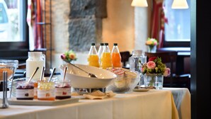 A breakfast buffet with various food items and beverages, including orange juice and milk, set against a backdrop of a stone wall and windows with curtains. - Romantik Hotel Schwan (Horgen)