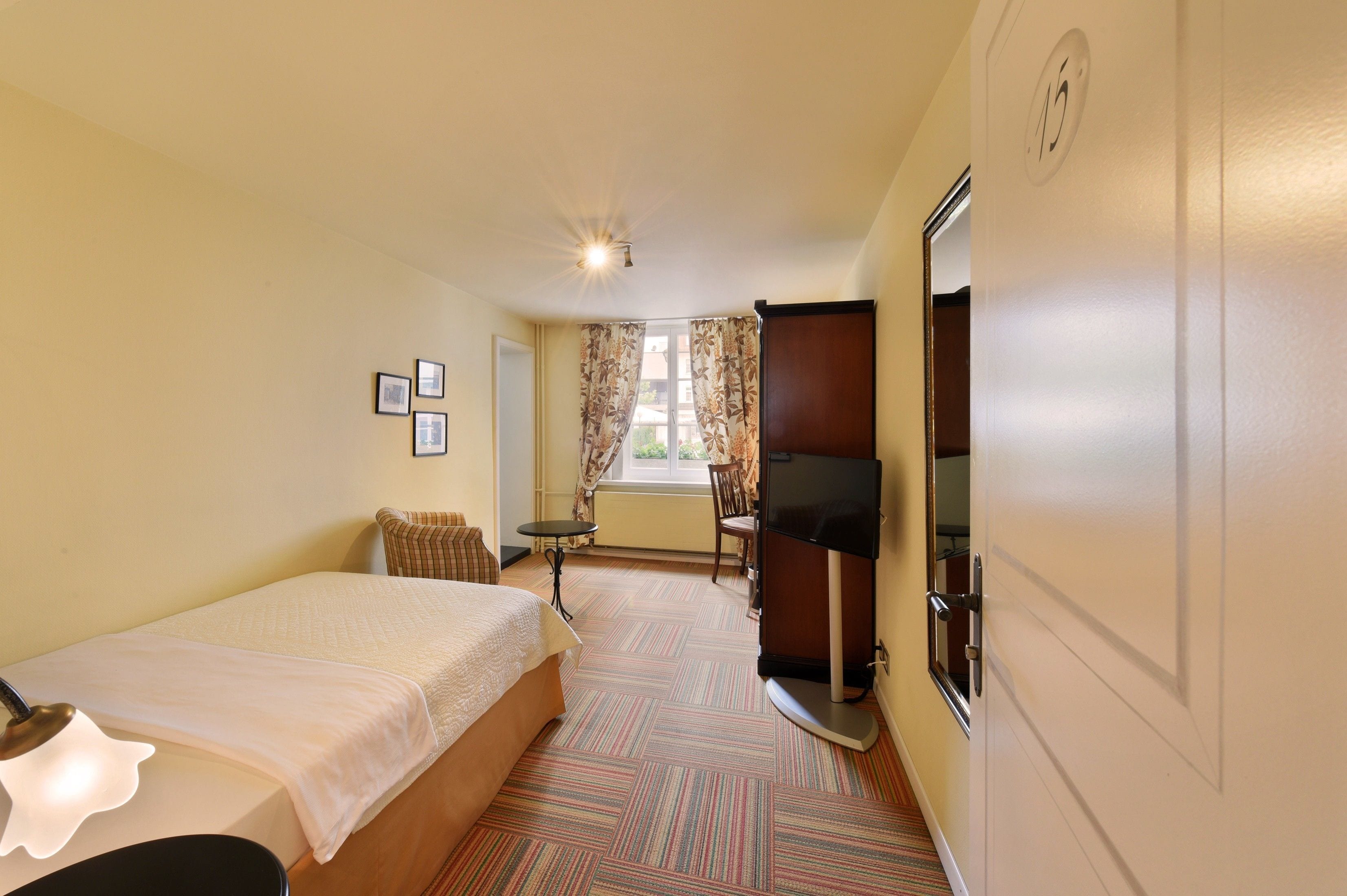 A hotel room with a bed, a desk, a television, and a window with curtains.