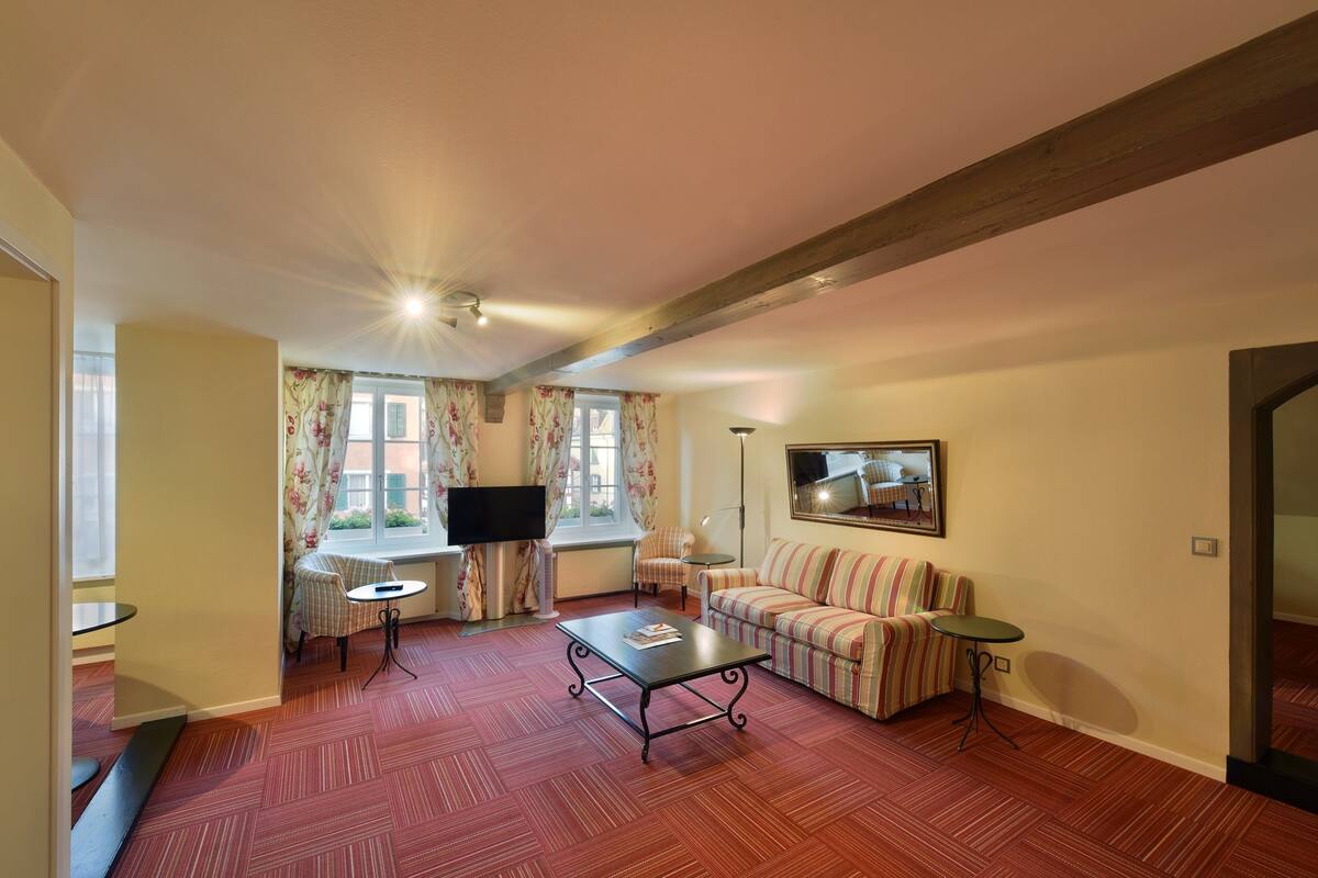 A living room with a sofa, a coffee table, a TV, and a window with curtains.
