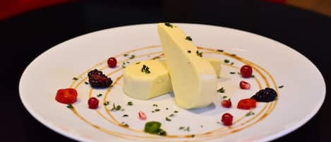 A dessert plate with a white plate, two yellow items, red berries, and green herbs.