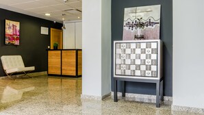 A lobby with a reception desk, a white chair, and a decorative cabinet with patterned tiles. - Hotel YIT Alcover (Granada)