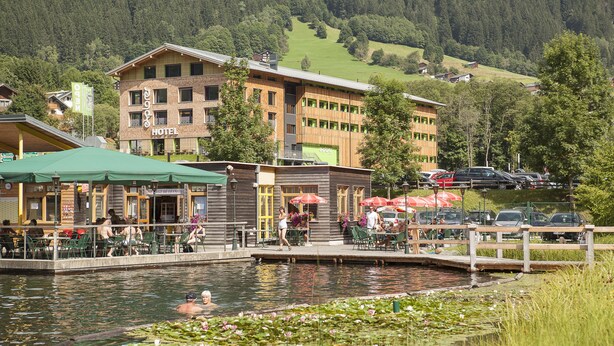 A hotel with a pool area, outdoor seating, and a view of the surrounding hills. - Explorer Hotel Montafon (Gaschurn)