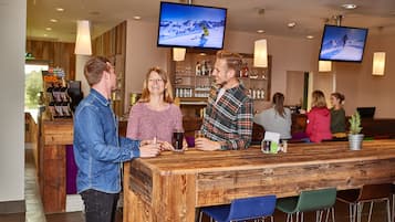 A bar area with wooden bar counter, multiple screens displaying content, and seating with chairs.