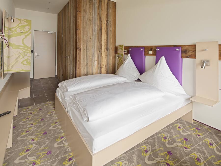 A modern hotel room with a bed, a TV, and a shower area.