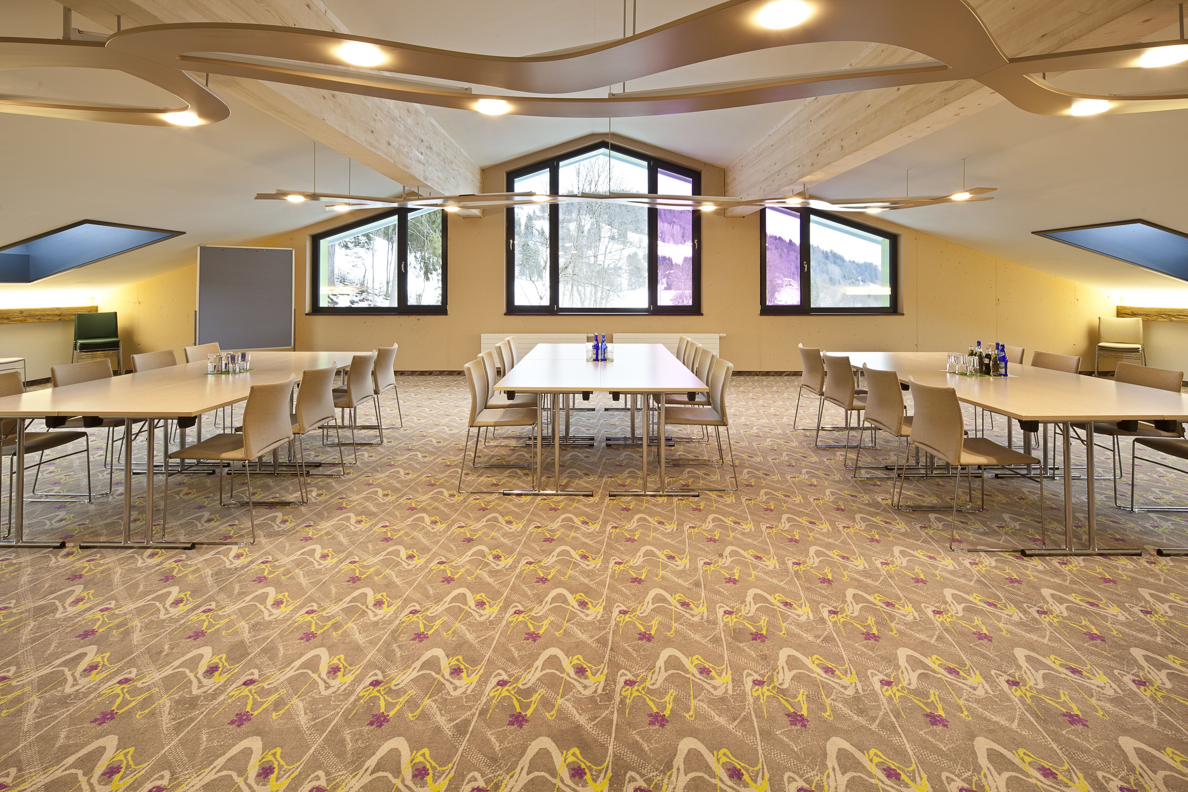 Kokoushuone, jossa on suuri pöytä, useita tuoleja ja suuret ikkunat, joista avautuu näkymä puistoon.