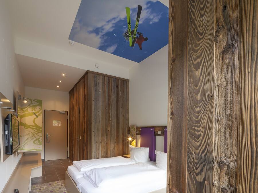 A hotel room with a large bed, wooden wardrobe, and a ceiling mural of a skier.