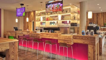 Zona de bar con mobiliario de madera, una pantalla de televisión y estantes llenos de botellas.