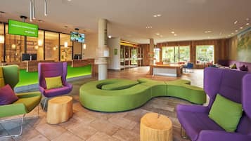 Un hall d’hôtel moderne comprenant un comptoir d’accueil, des espaces de détente et un écran de télévision diffusant un message de bienvenue.