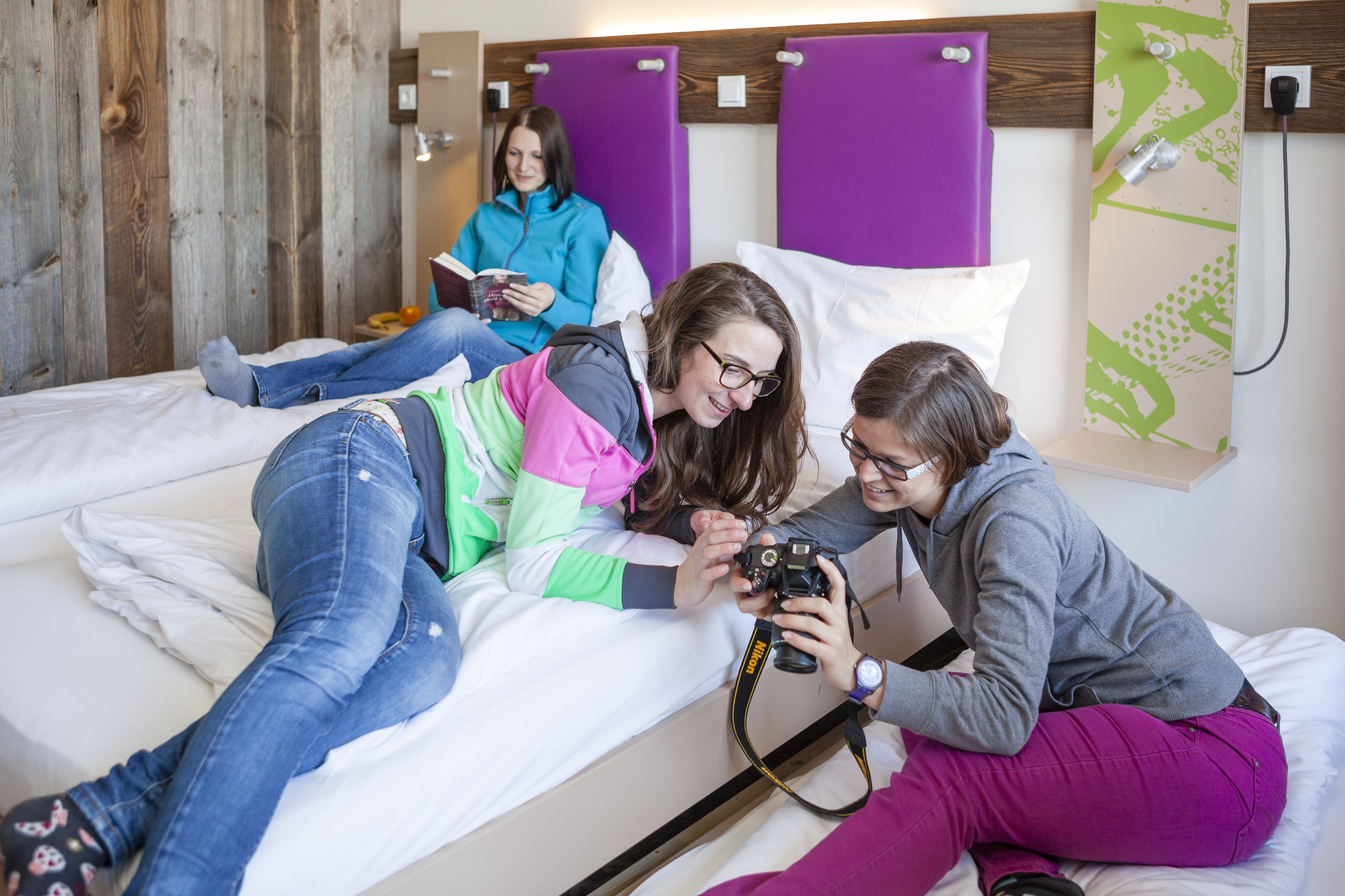 A room with a bed, wooden wall paneling, a purple headboard, and a wall-mounted shelf with a green abstract design.