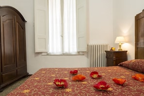 A bedroom with a bed, a nightstand, a dresser, a window with curtains, and a radiator. - Albergo Tre Donzelle (Siena)