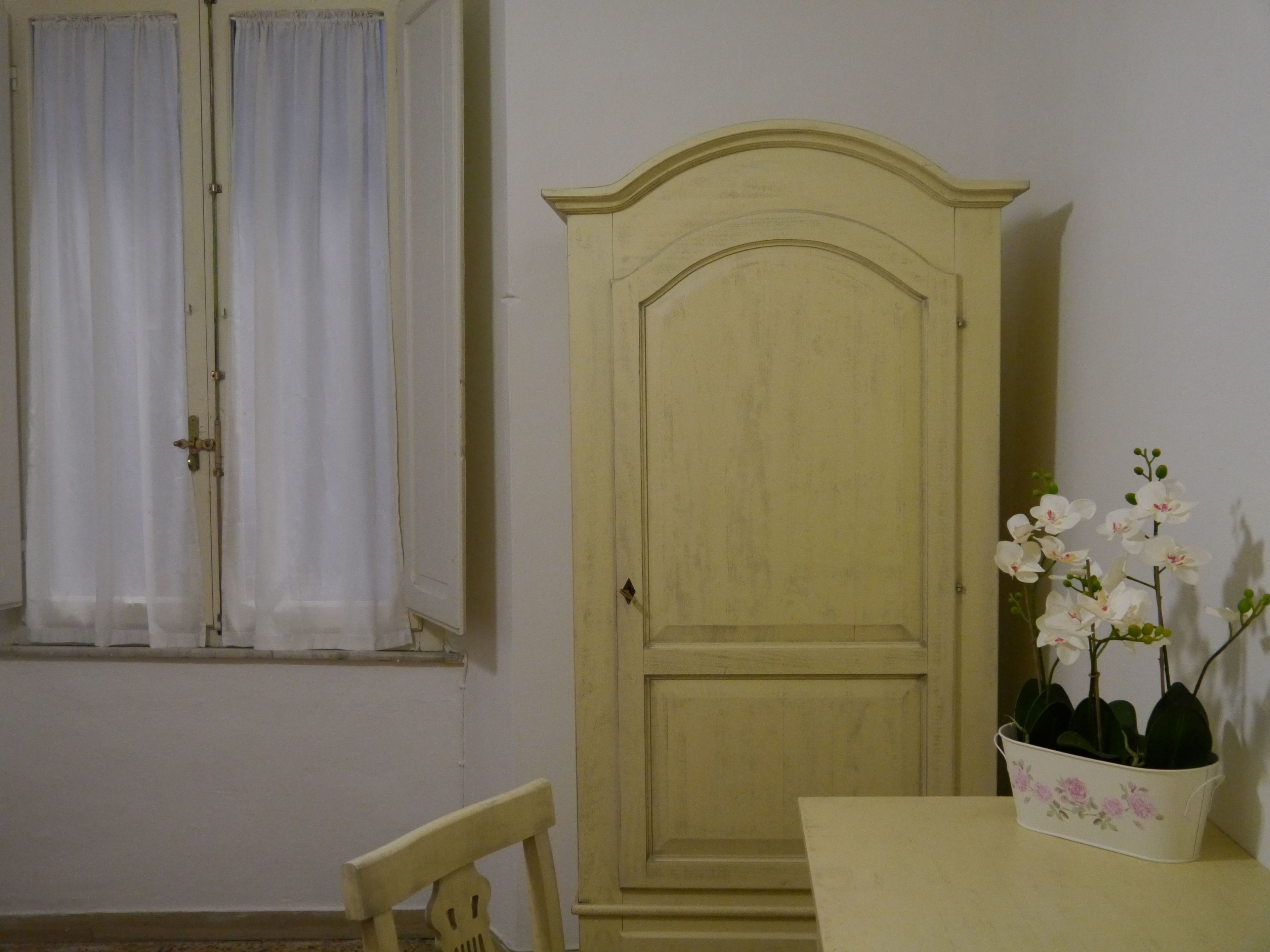 Une pièce comprenant un meuble en bois, une chaise, une table et une fenêtre avec des rideaux.