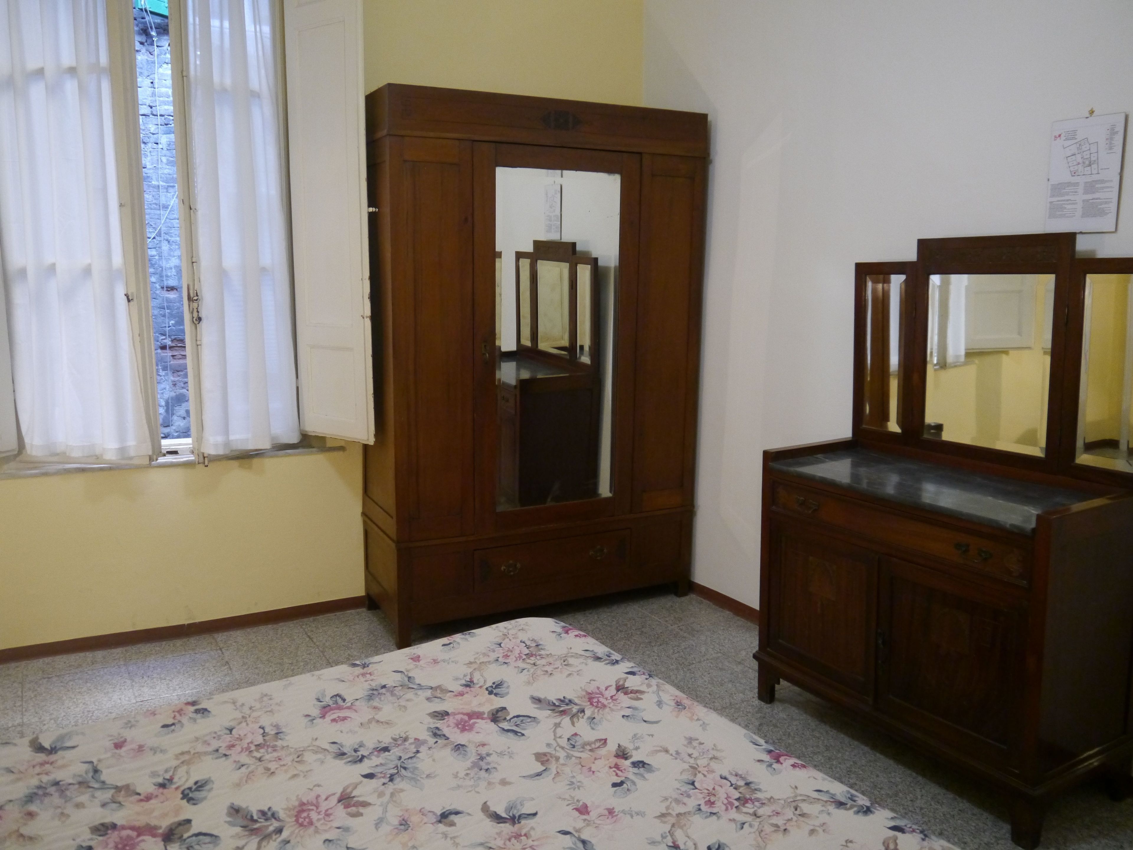 Un dormitorio con una cama, un armario de madera, un tocador con espejo y una ventana con cortinas.