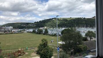 A view of a marina with boats, a grassy field, and a hill with buildings in the background.