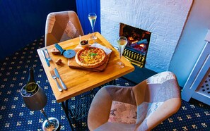 A cozy dining area with a pizza on a wooden table, a bottle of wine, and a fireplace in the background. - Ship in Dock Inn (Dartmouth)