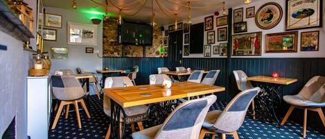 A restaurant interior with wooden tables and chairs, a patterned floor, and various framed pictures on the walls.