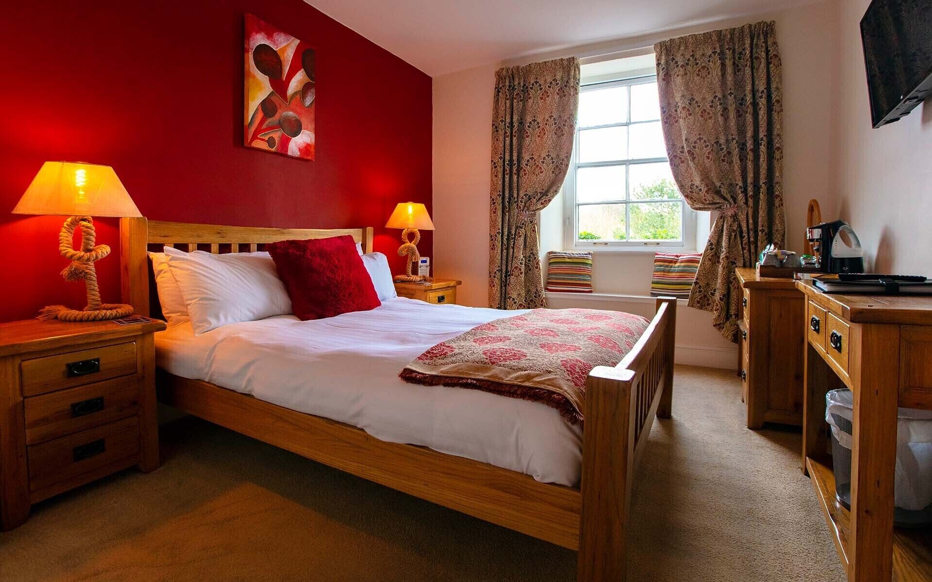 A hotel room with a wooden bed, red walls, and a window with curtains.
