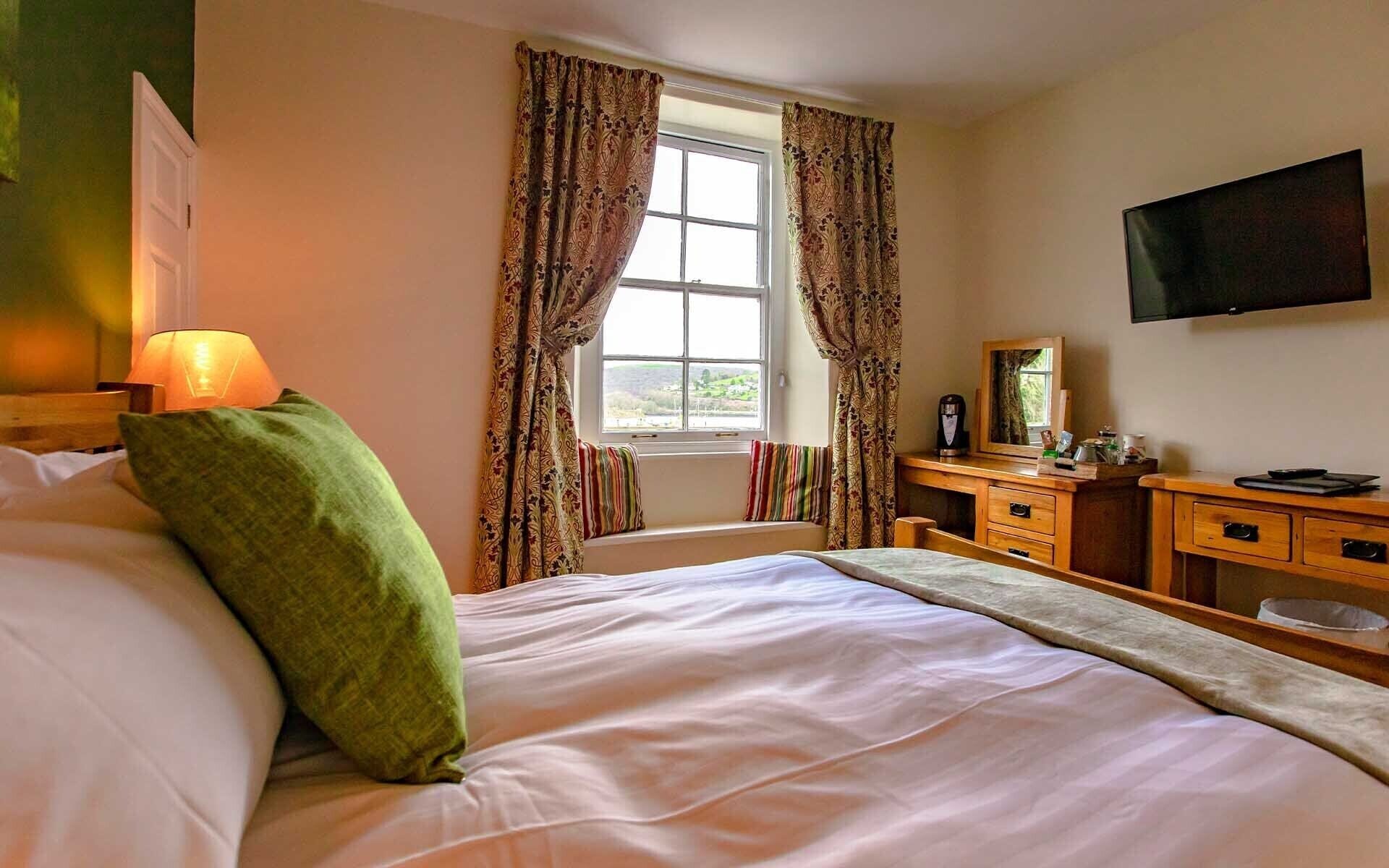 Habitación de hotel con cama, escritorio, silla, televisor y ventana con cortinas.