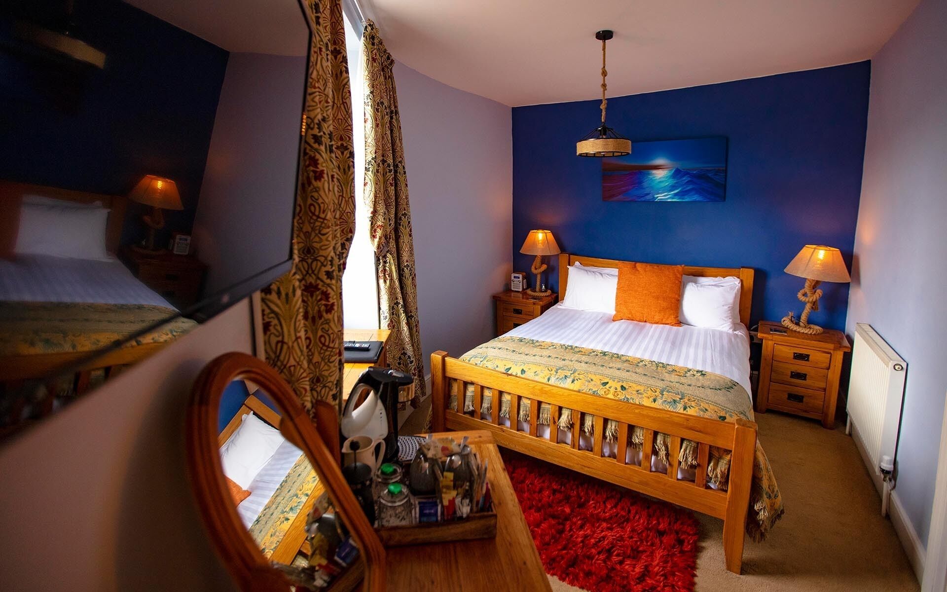 Ein Schlafzimmer mit einem Bett, zwei Nachttischen, einem Spiegel, einem roten Teppich und einem Bild an der Wand.