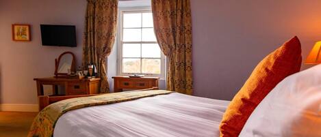 A bedroom with a bed, a desk, a chair, a television, and a window with curtains.