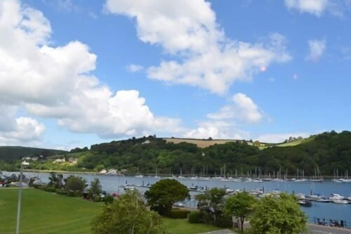 A marina with boats docked, surrounded by greenery and hills.