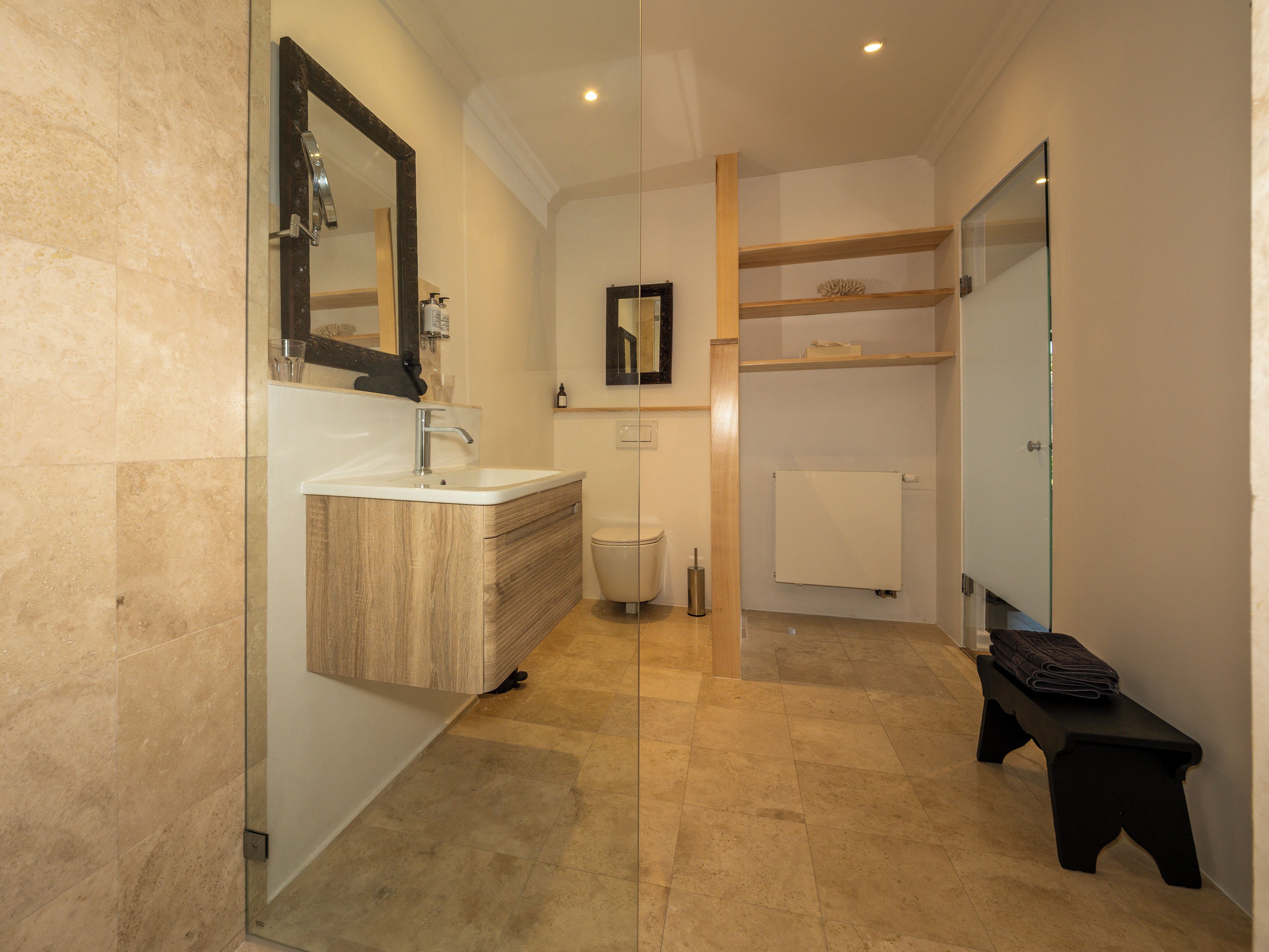 A modern bathroom with a glass shower enclosure, a wooden vanity, a toilet, and a bench.