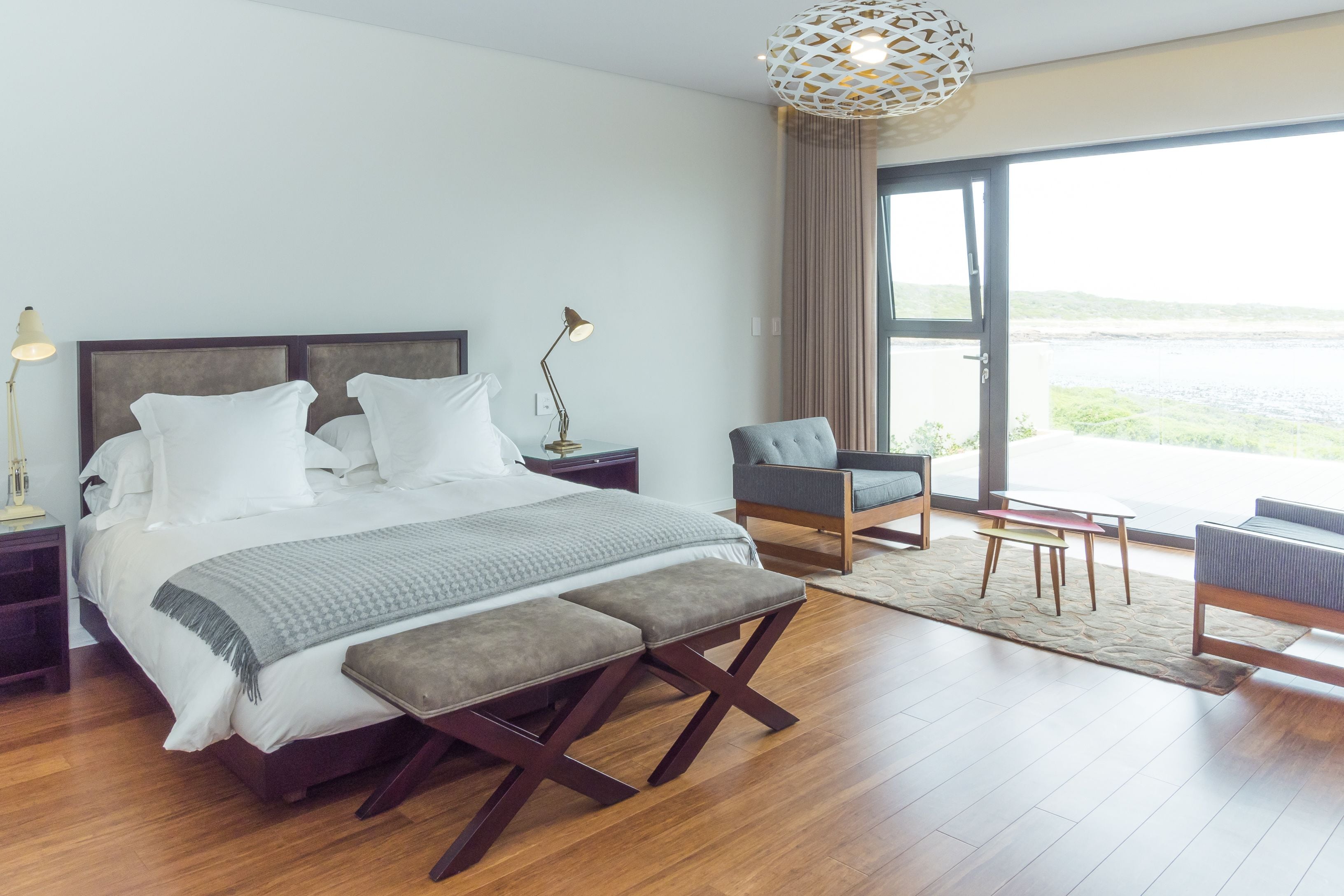 A modern bedroom with a large bed, bedside tables, a bench, and a view of the outdoors.