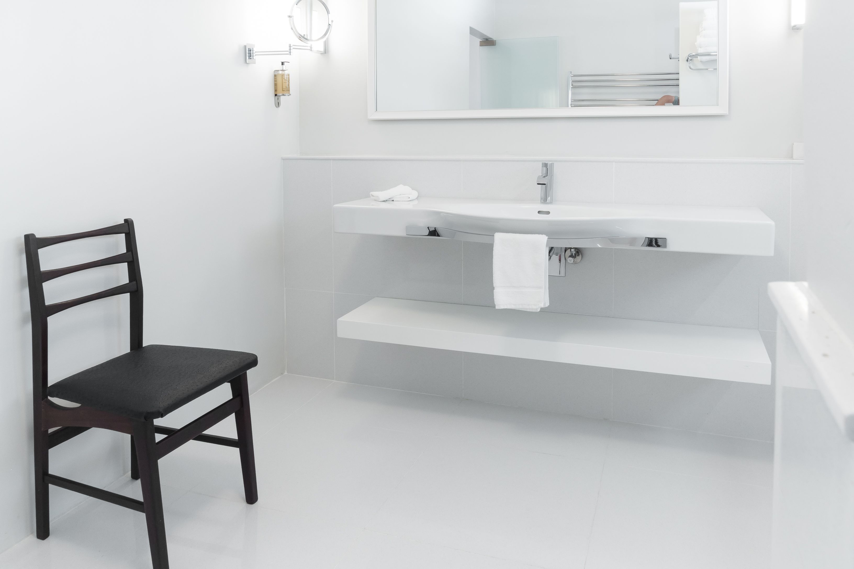 Un bagno moderno con una sedia in legno scuro, un lavandino bianco e uno specchio sopra.