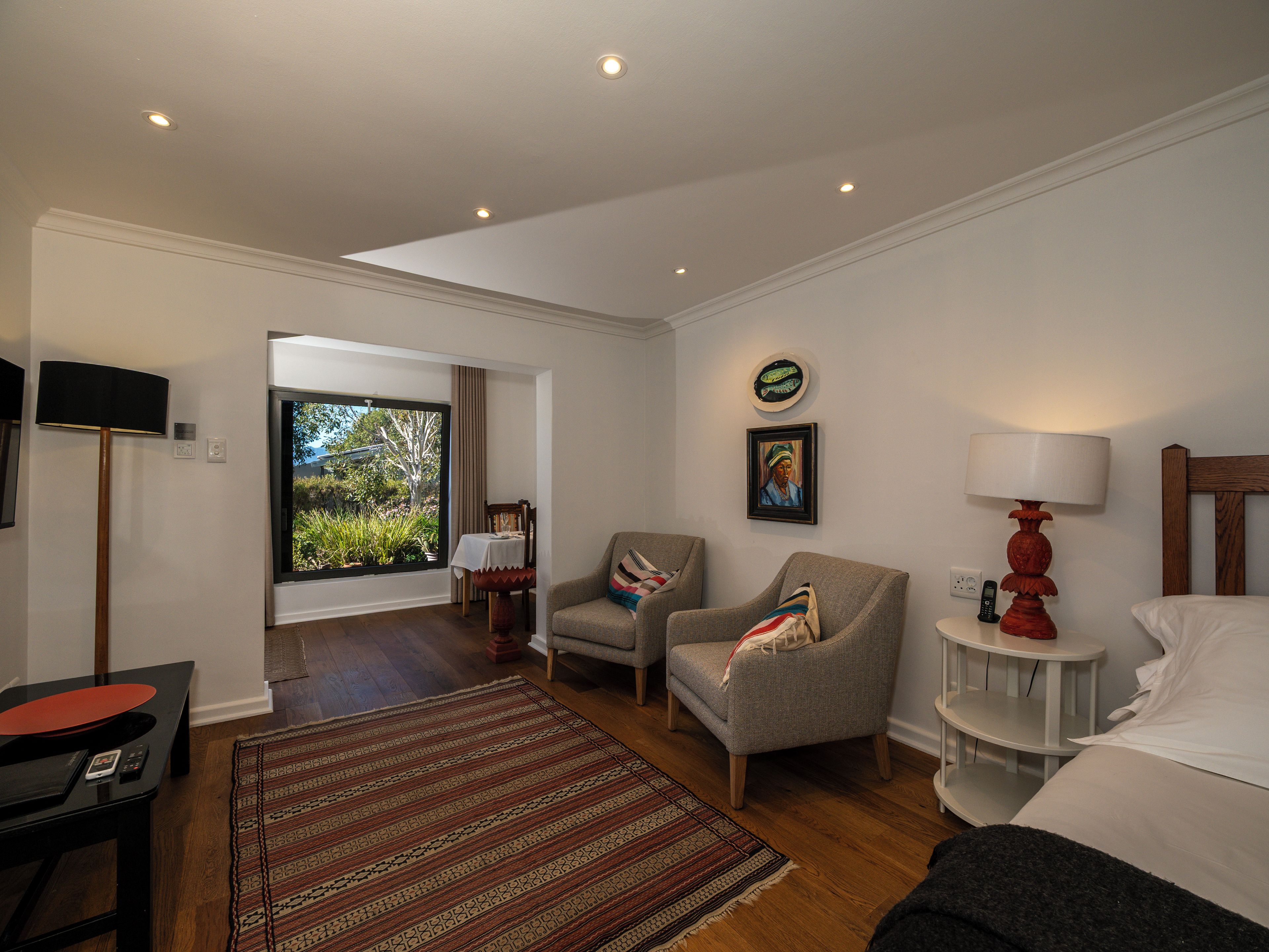 Une chambre d’hôtel avec une grande fenêtre, un lit, une chaise, une table et une lampe.