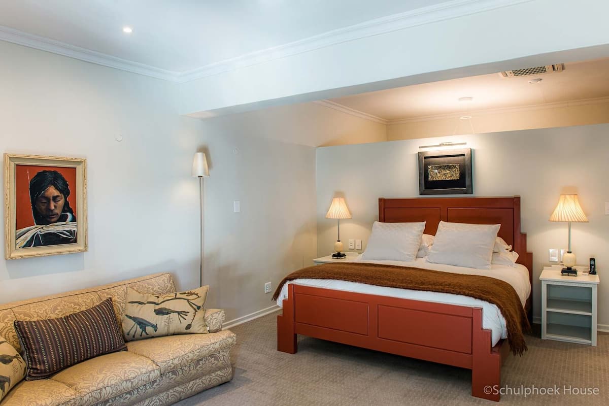 A bedroom with a bed, bedside tables, a lamp, a sofa, and a framed picture on the wall.