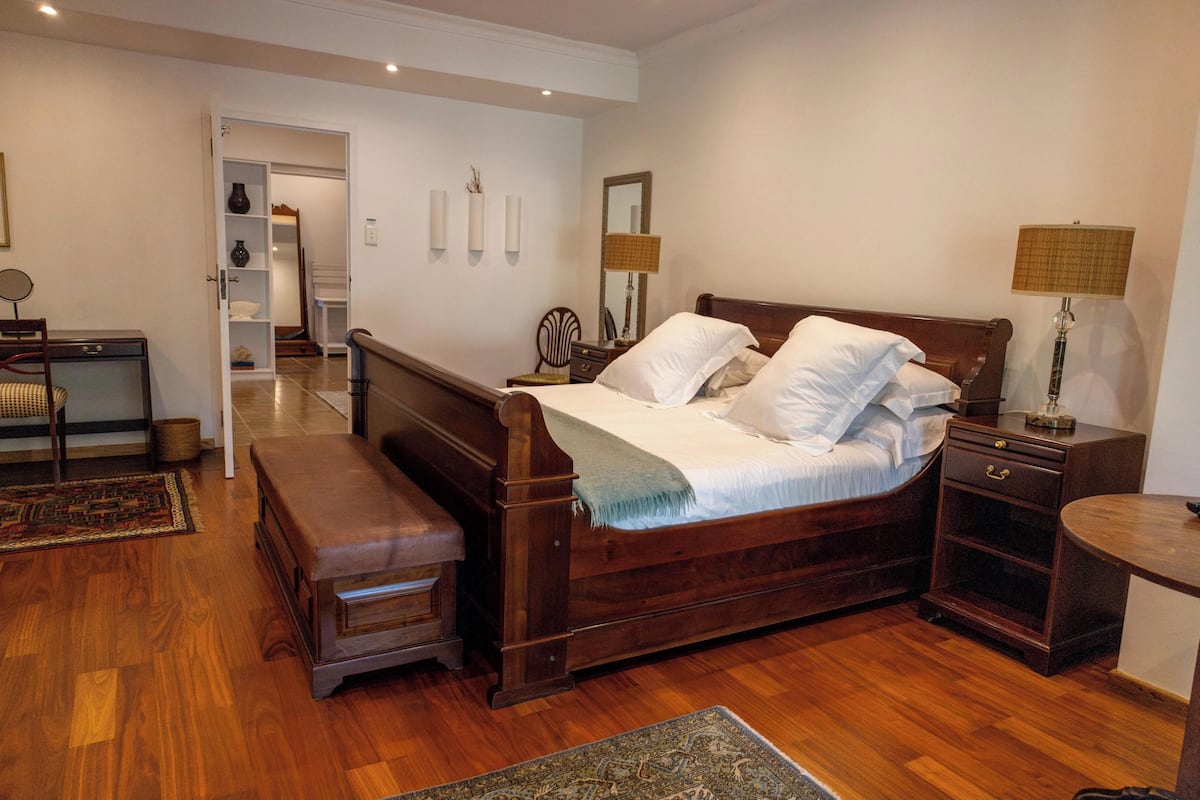 A bedroom with a wooden bed, bedside tables, a bench, and a desk with a chair.