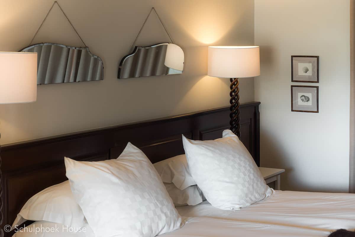 A neatly made bed with white linens and pillows, a dark wooden headboard, and two wall-mounted lamps.