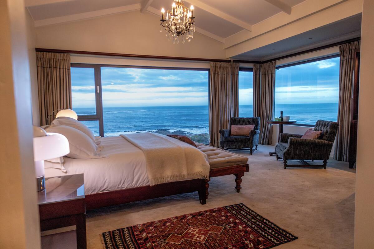 A bedroom with a large bed, a sitting area with a view of the ocean, and a chandelier.
