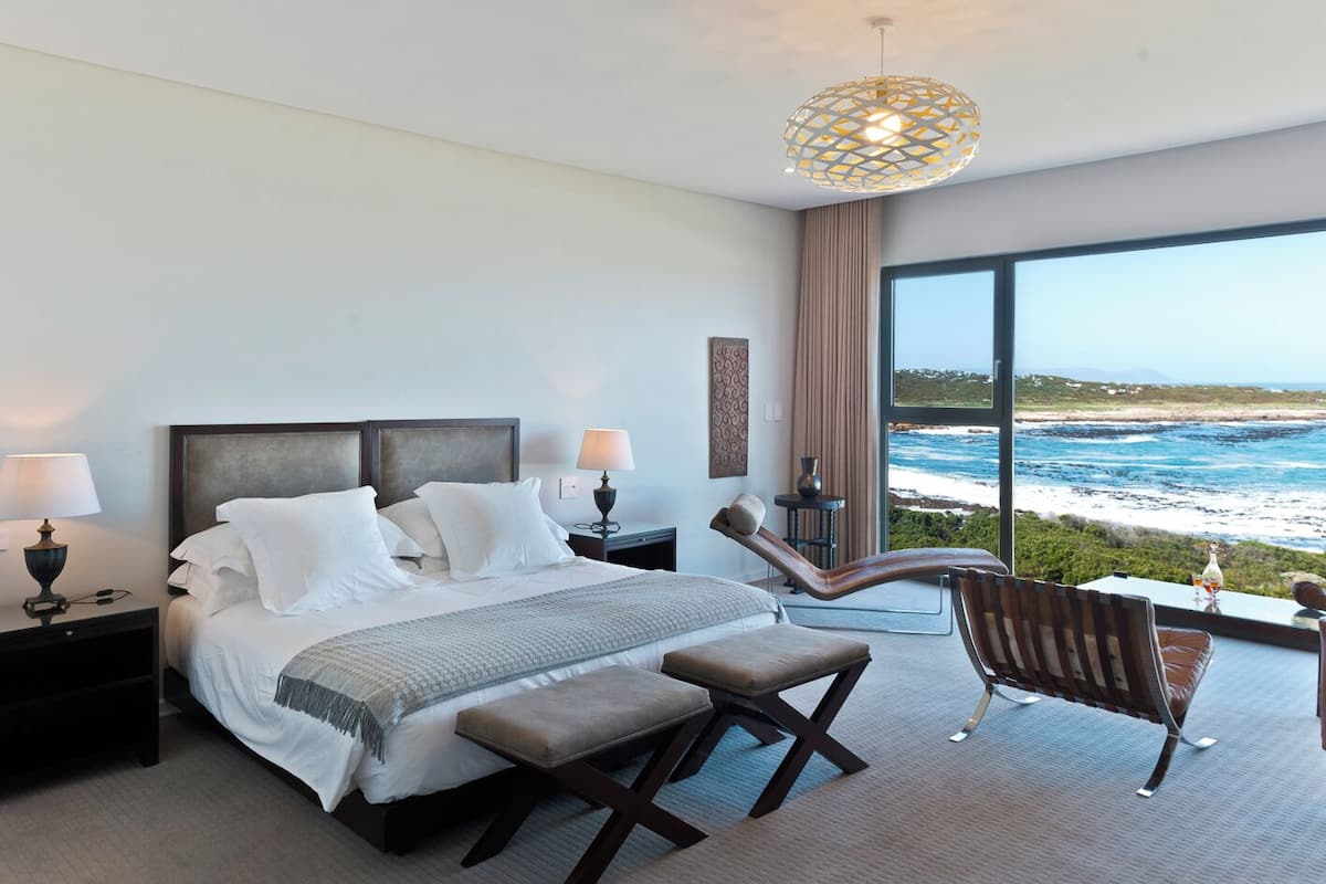 A modern hotel room with a large bed, a chaise lounge, and a view of the ocean.