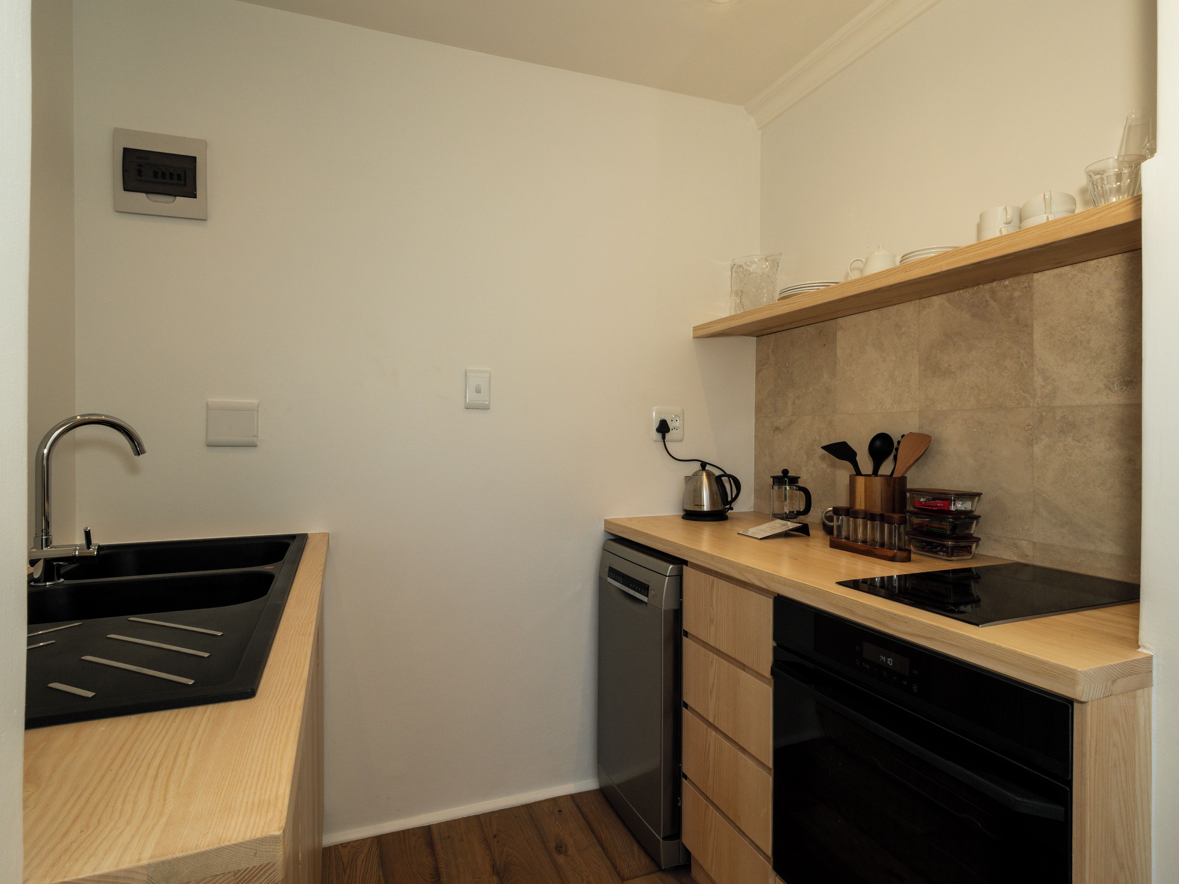 A compact kitchen with a sink, dishwasher, and a countertop with a kettle and utensils.