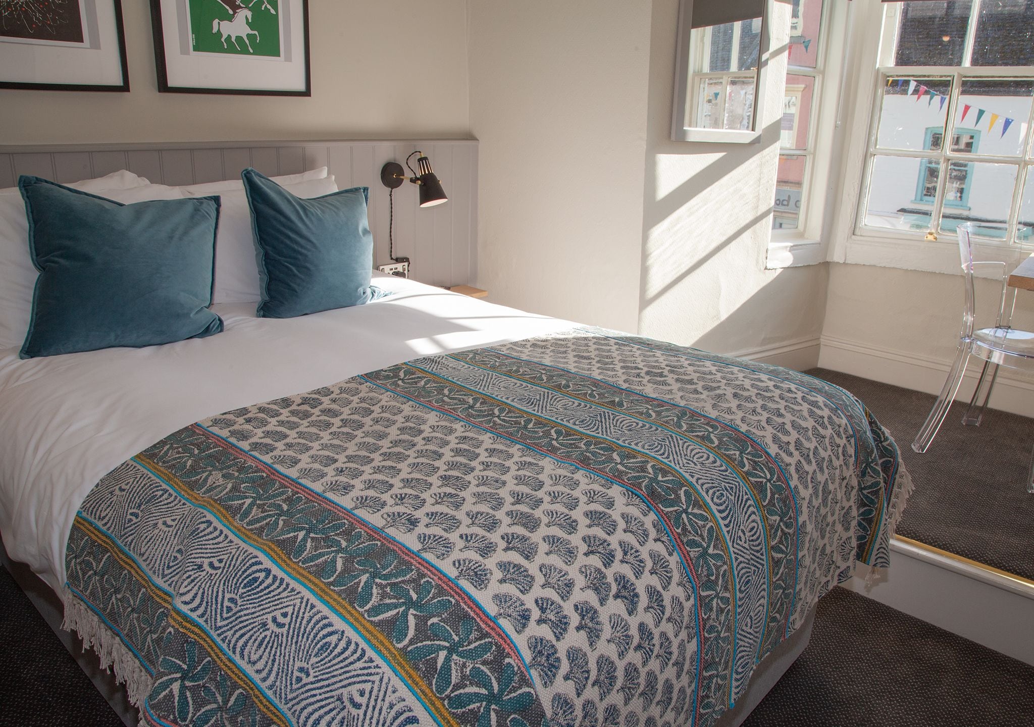 A neatly made bed with a patterned bedspread, a bedside lamp, and a clear view of the window with a view of the outside.