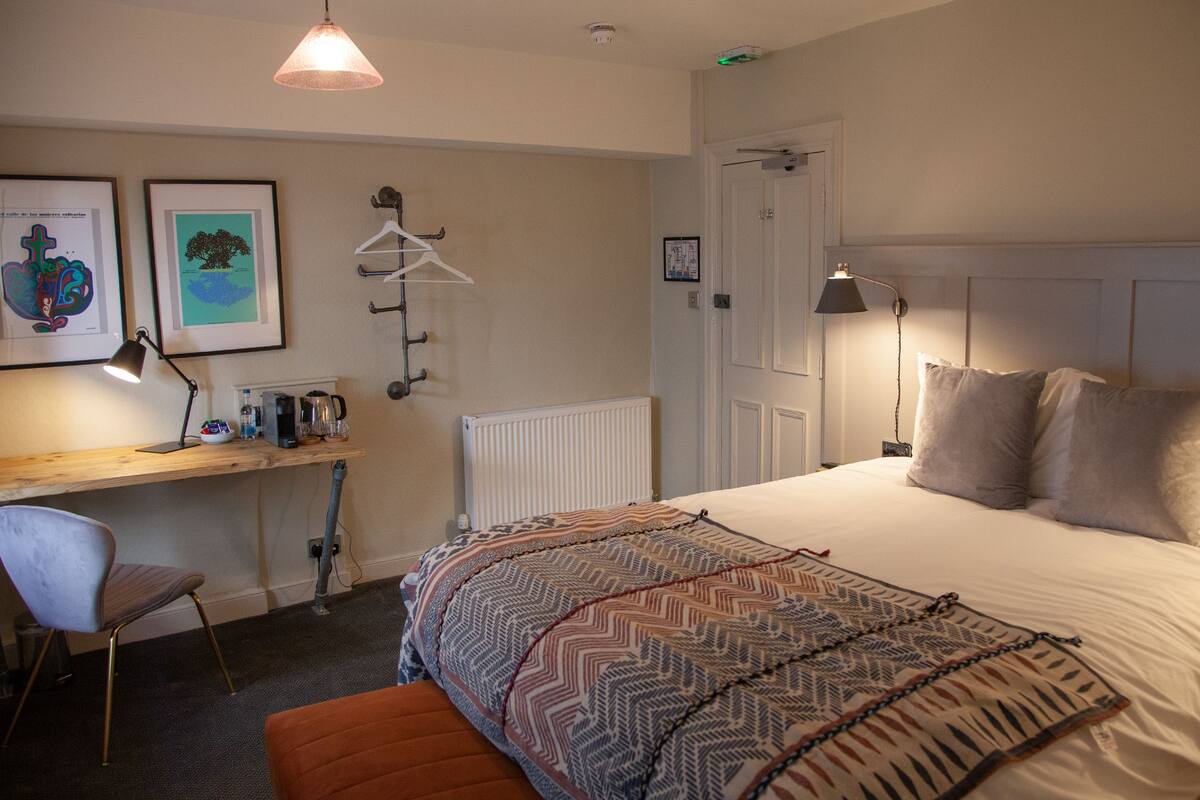A bedroom with a bed, a desk with a chair, a radiator, and framed pictures on the wall.