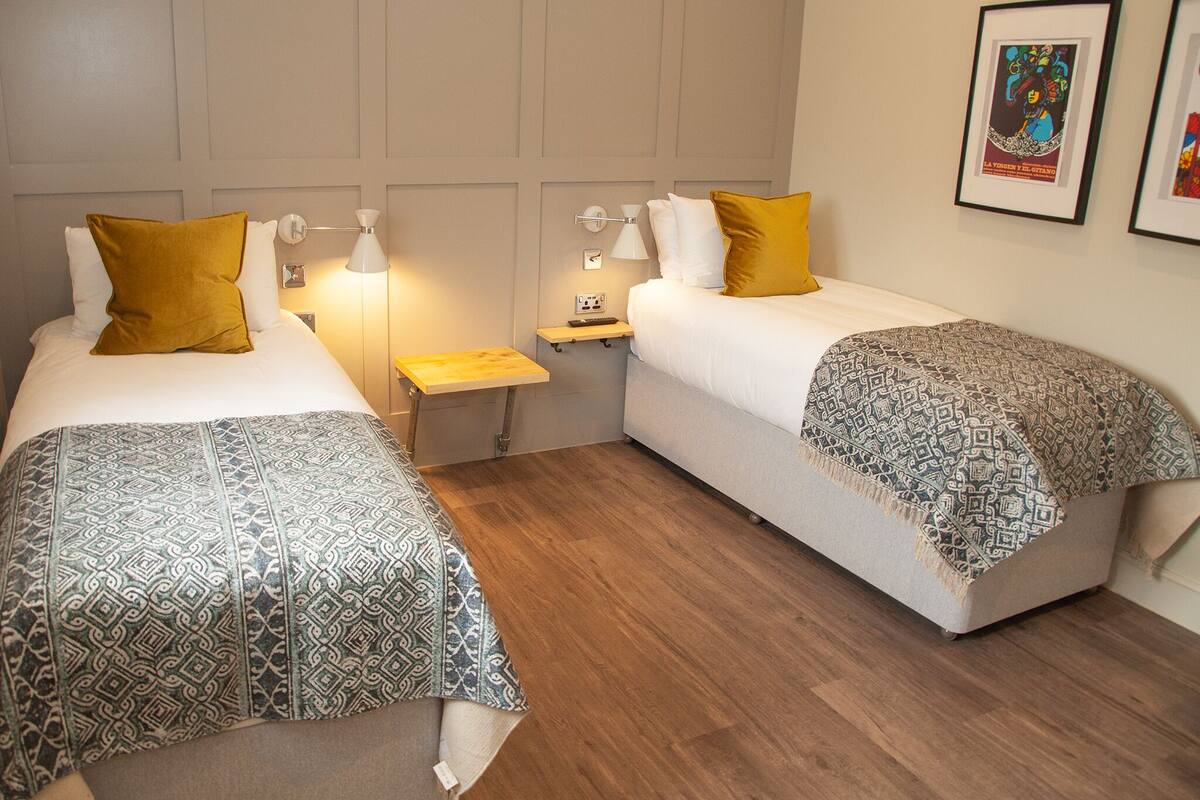 A room with two single beds, each with patterned bedding and a bedside table with a lamp.