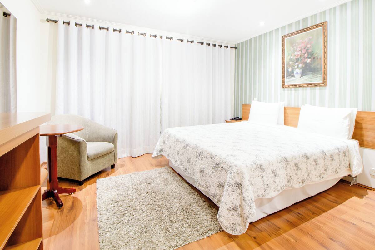 Une chambre d’hôtel avec un lit, un bureau, une chaise, une table de chevet et un tableau au mur.