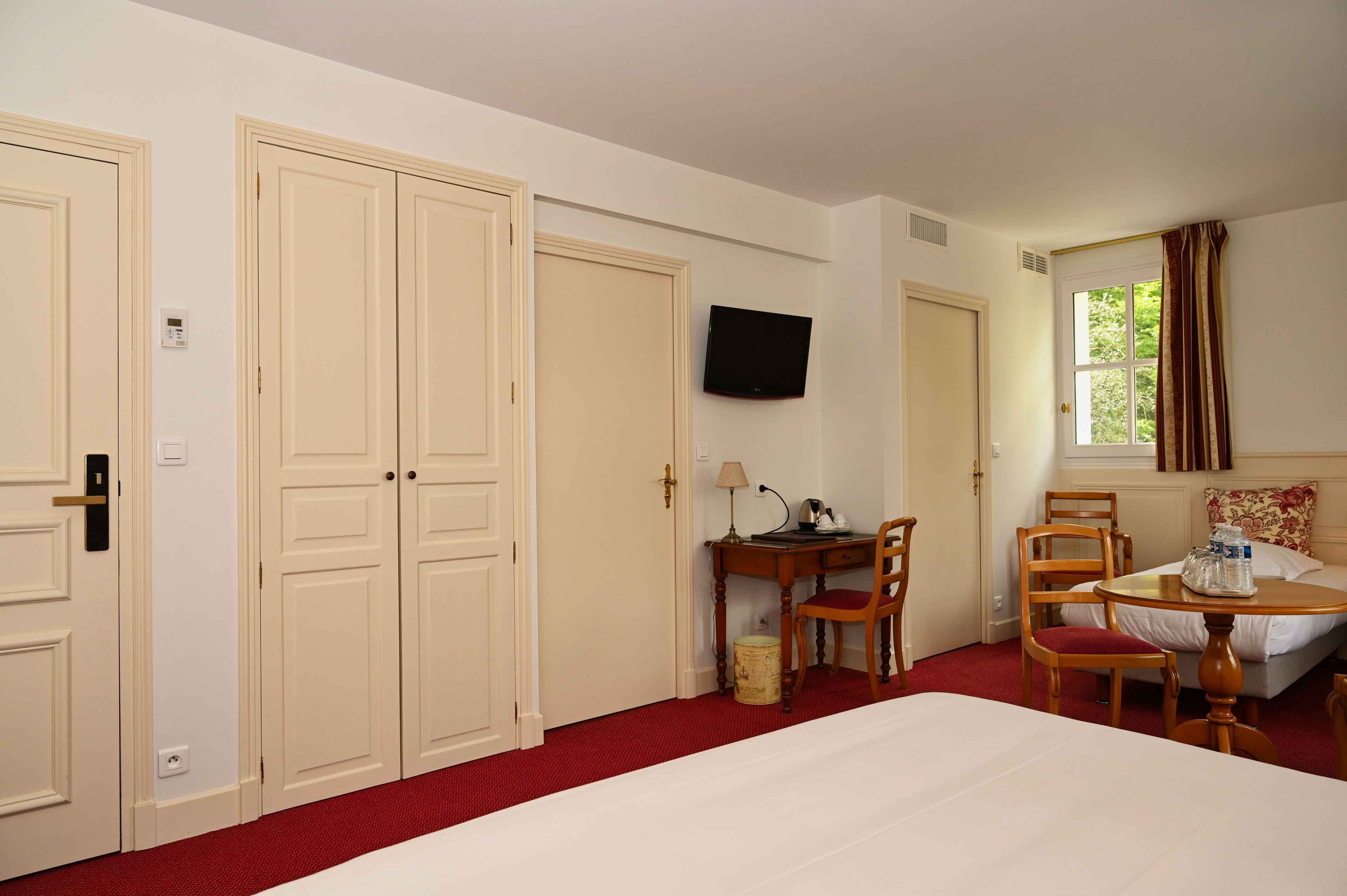 Una habitación de hotel con cama, escritorio con silla, televisor y ventana con cortinas.