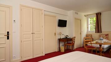 Una habitación de hotel con cama, escritorio con silla, televisor y ventana con cortinas.